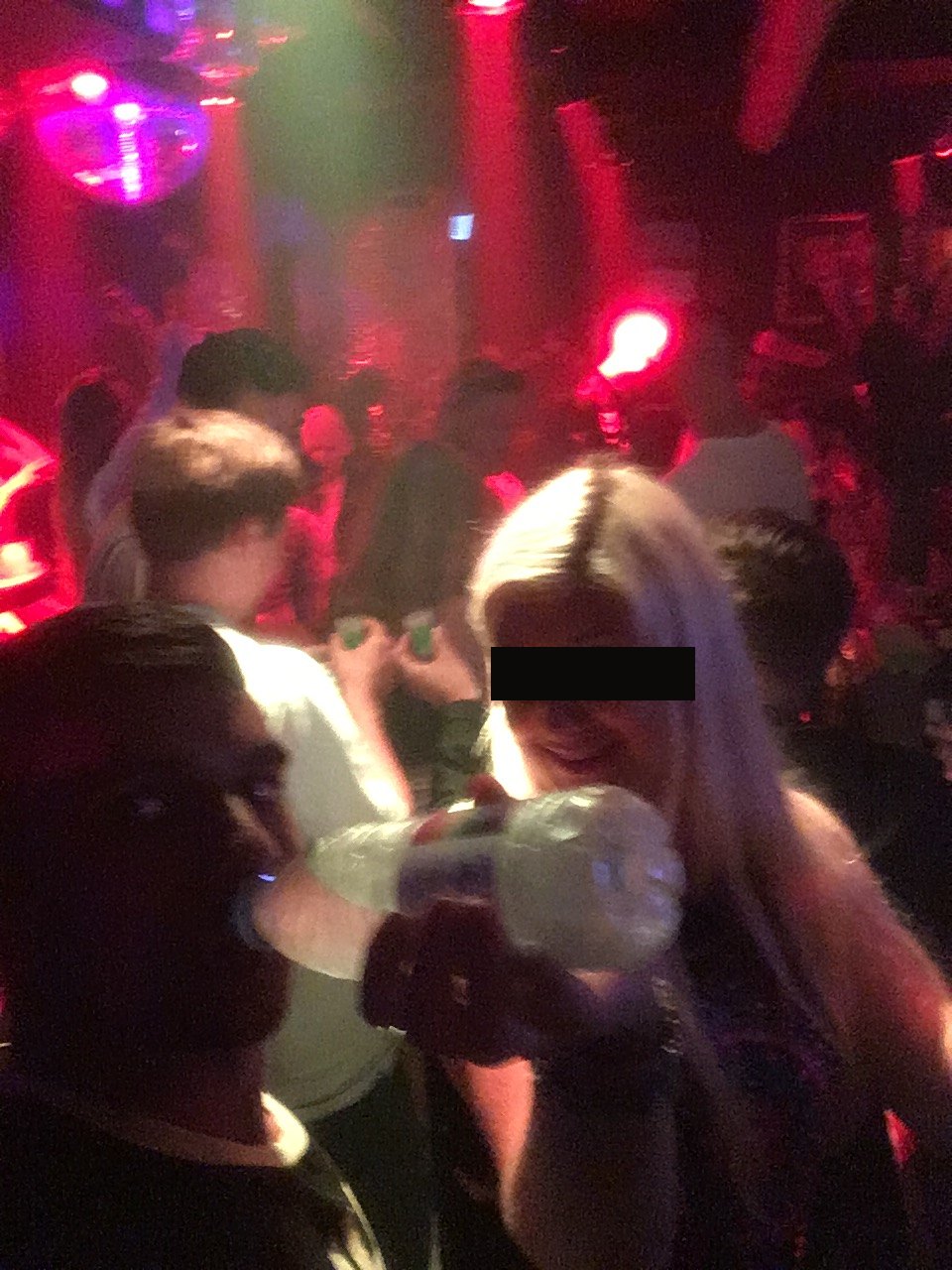 Gin drinking from a bottle on a crowded dance floor, other faces blurred