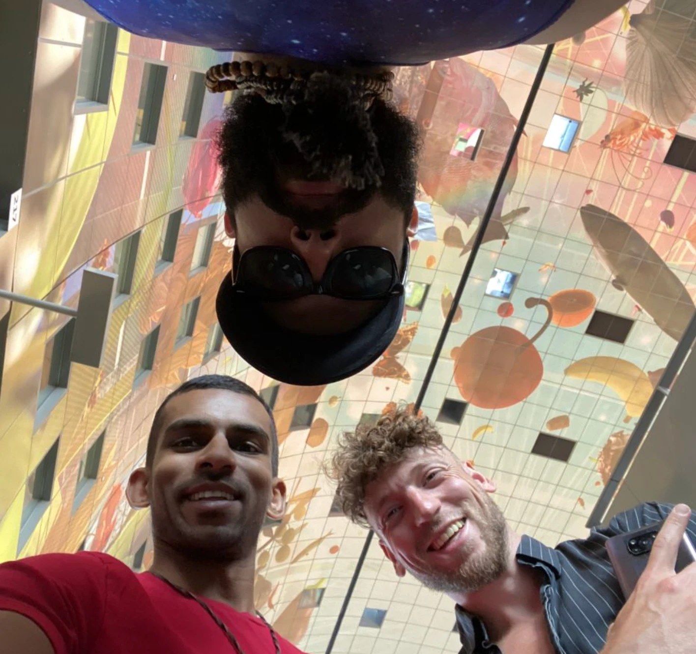 Gin and two friends smiling under the painted ceiling of the Markthal in Rotterdam